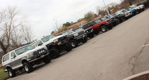 1979 Ford Bronco - A row of Ford Broncos, predominantly from the 1990s, are parked in a lot under an overcast sky.