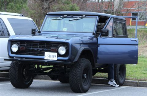 1979 Ford Bronco - This blue Ford Bronco has its driver's door ajar, revealing a license plate that reads 'A STUD69'.