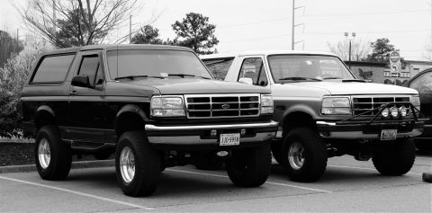 1979 Ford Bronco - Two Ford Broncos, likely from the early to mid-1990s, are parked together in a lot.