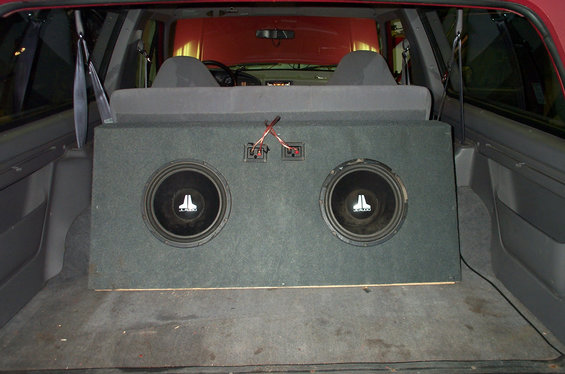 Two JL Audio subwoofers in a carpeted box mounted in the rear cargo area of a red SUV