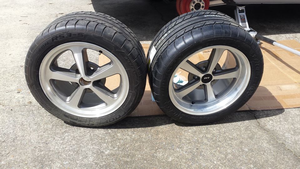 Two aftermarket wheels with tires, one has an SVT center cap. A jack is visible in the background