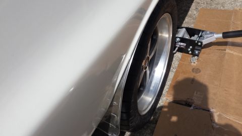 1976 Ford Ranchero - A low-angle, close-up side view of a white vehicle's rear fender and tire. A silver hydraulic floor jack is positioned under the fender, re…
