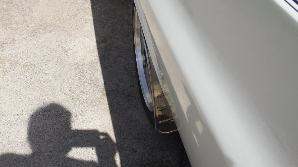 Side view of a white vehicle's rear wheel well with a custom mud flap.