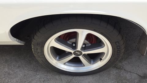 1976 Ford Ranchero - A close-up view of the front passenger side wheel of a white vehicle, featuring a silver five-spoke SVT wheel with a Cooper tire. Red brake…
