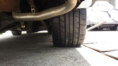 1976 Ford Ranchero - Close-up view of a vehicle's rear tire and exhaust system, with another car covered in the background.