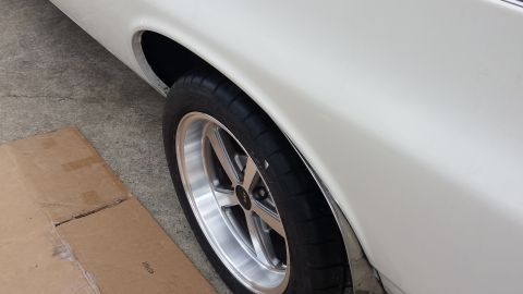 1976 Ford Ranchero - A close-up, side-angle view of the rear wheel well and fender of a white vehicle, possibly a classic car or truck, with a silver multi-spok…