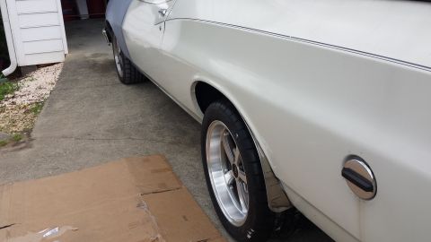 1976 Ford Ranchero - A close-up side view of a white classic car, possibly a Ford Ranchero, showing the rear wheel and part of the fuel door. The car is parked…