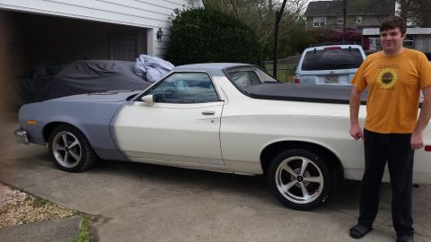 1976 Ford Ranchero - A man stands next to a white and gray Ford Ranchero with aftermarket wheels parked in a driveway. Another vehicle is covered with a gray ta…