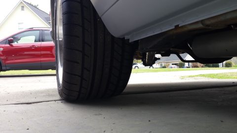 1976 Ford Ranchero - Low angle view of the rear tire and undercarriage of a vehicle, showing the exhaust system and suspension components. A red SUV is visible…