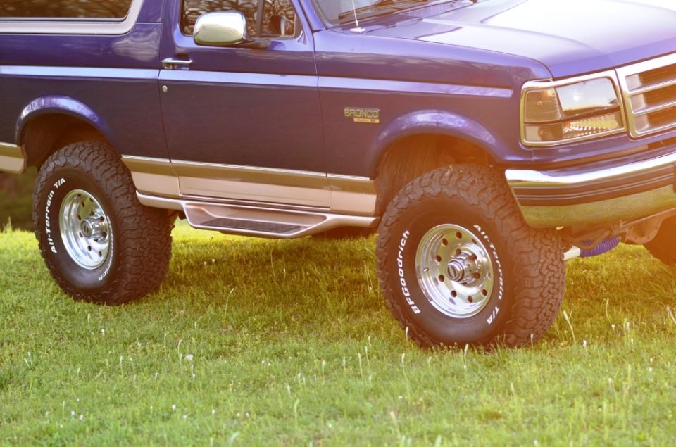 Dark blue 1996 Ford Bronco front driver's side view, showing tires, running boards, and chrome details on grass.
