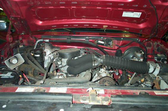 Engine bay of a red Ford truck showing V8, air intake ducting and master cylinder