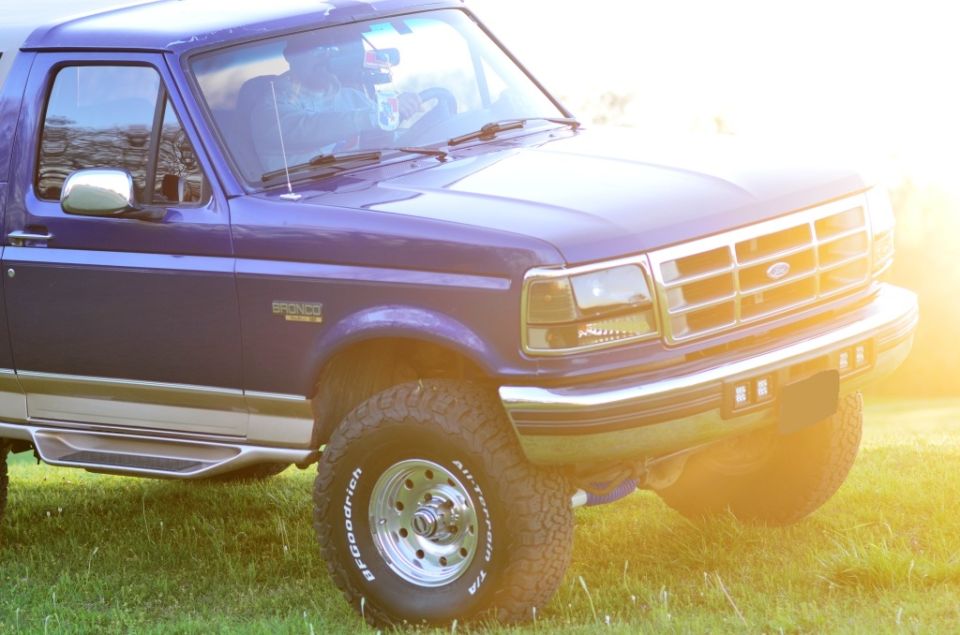 Purple 1996 Ford Bronco with chrome accents and BFGoodrich All-Terrain tires, parked in a grassy field during sunset.
