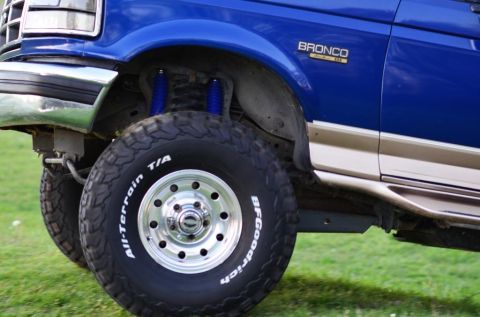 1996 Ford Bronco - The side of a blue SUV is shown, focusing on the wheel and lower body panel.