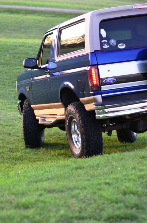 1996 Ford Bronco - Rear quarter view of a lifted Ford Bronco with aftermarket wheels and tires parked on a grassy hill.