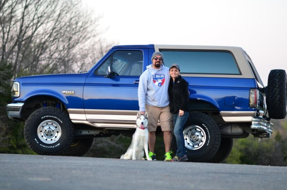 1996 Ford Bronco with two people and a husky dog standing next to it