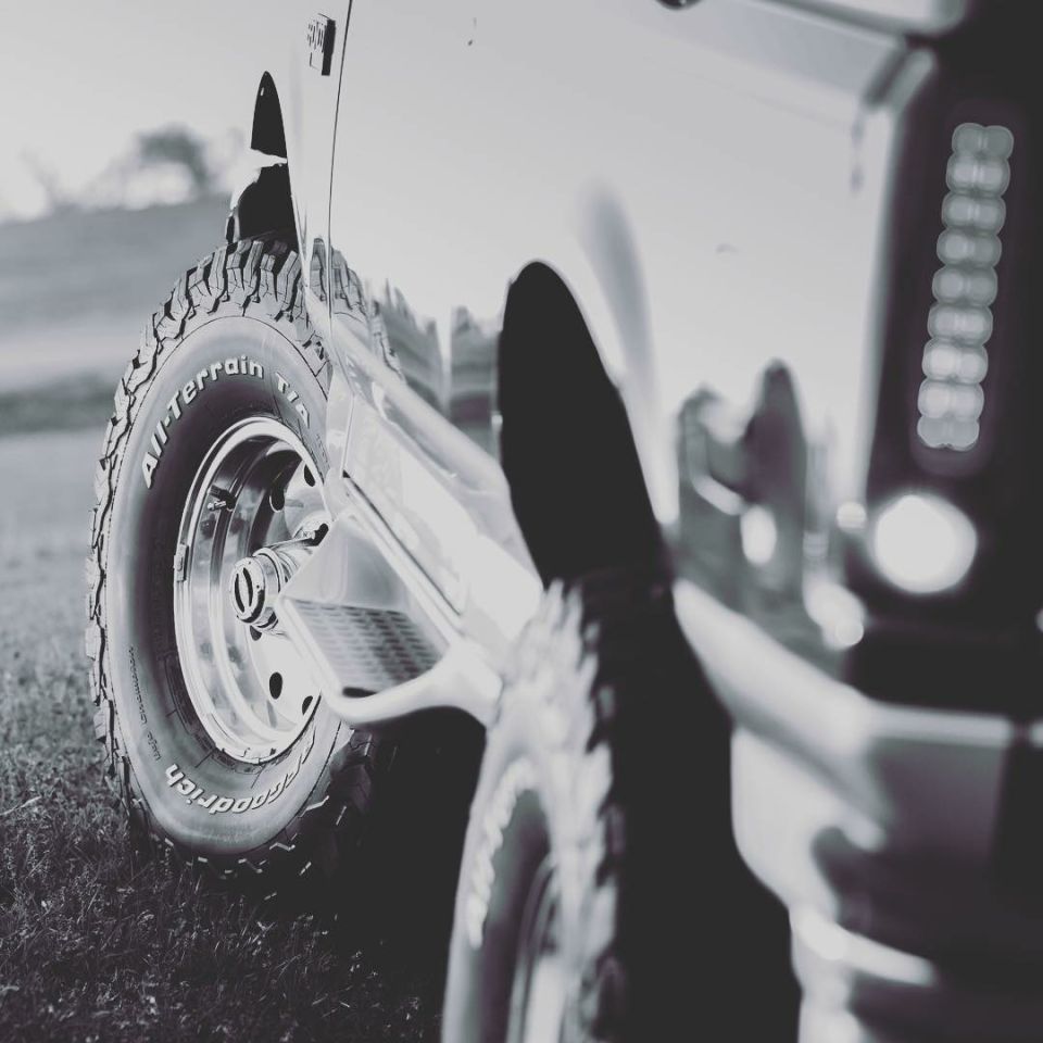 Close-up of a BFGoodrich All-Terrain tire on a classic SUV, black and white.