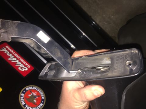 1995 Ford Bronco - A hand holds a black plastic vehicle part, possibly a door handle assembly, against a black vehicle. A red sticker with white text that rea…