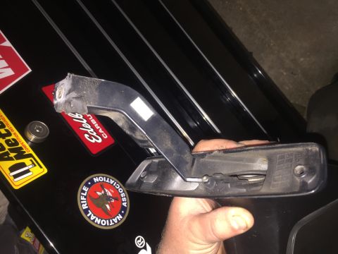 1995 Ford Bronco - A person is holding a black plastic door handle assembly with visible internal mechanisms and springs. The handle is resting on a black sur…