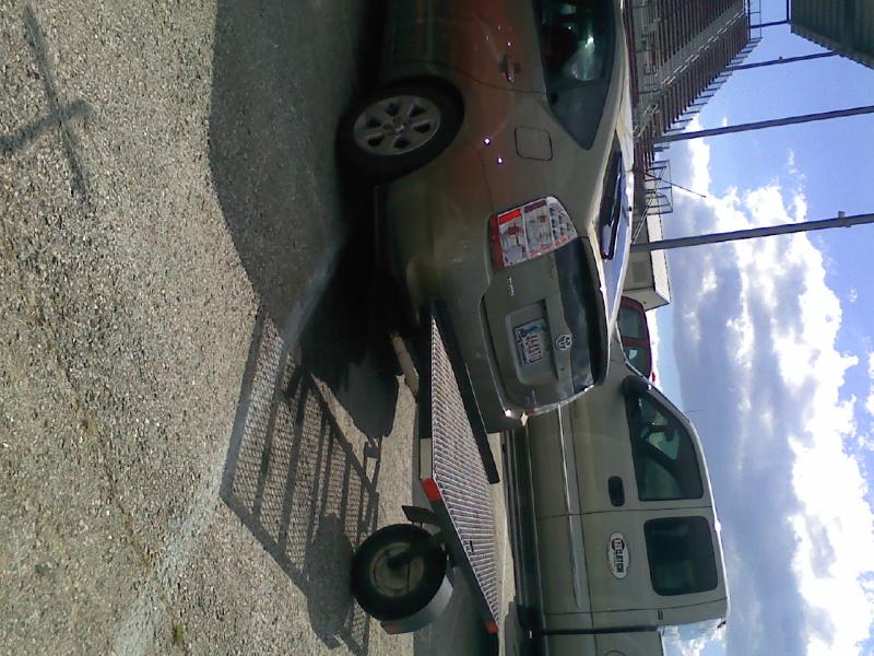 Gold Toyota Prius with a trailer attached, parked next to a silver pickup truck.
