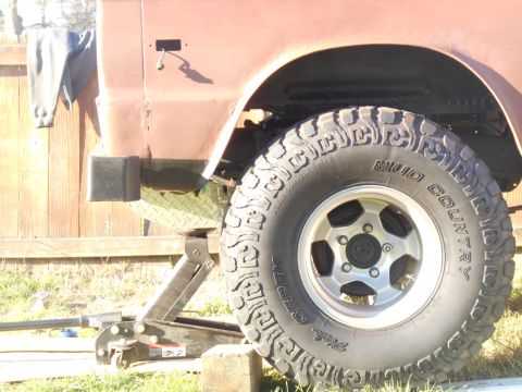 1972 Ford Bronco - A close-up view of the front passenger side tire and fender of a vintage vehicle, possibly a Ford Bronco, supported by a hydraulic jack. Th…