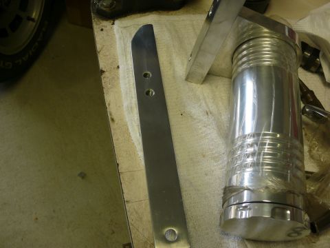 Polished aluminum piston and a flat metal piece with holes.