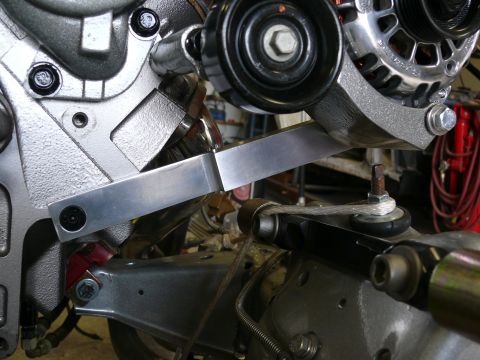 Polished aluminum bracket connecting engine block to alternator mount in an engine bay.