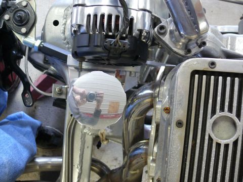 Polished engine bay with chrome headers and a circular mirror reflecting the photographer.