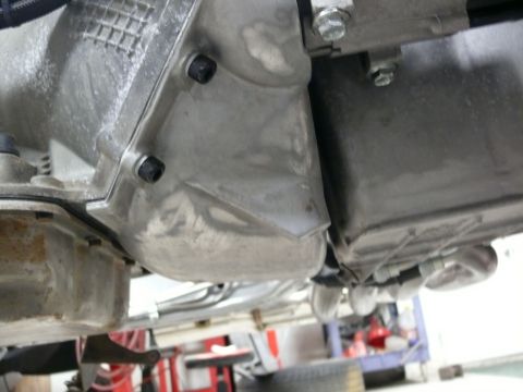 Underside of vehicle transmission and oil pan with visible bolts and metal components.