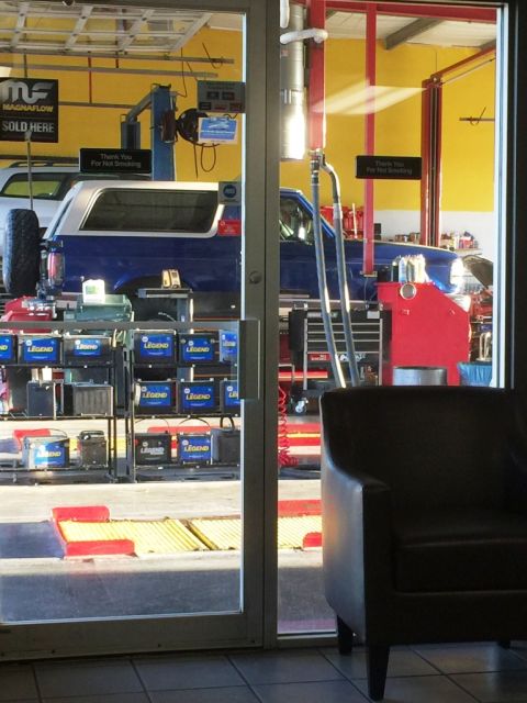 1996 Ford Bronco - A blue Ford Bronco is seen in an auto repair shop, with a white top and spare tire mounted on the back.