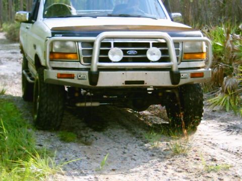 1995 Ford Bronco - This white Ford truck, likely from the early 1990s, is equipped with a heavy-duty bull bar and off-road tires.