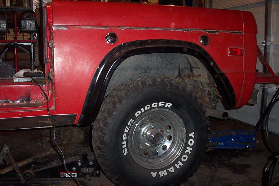 Red early Bronco rear quarter on jack stands with a Yokohama Super Digger tire on a slotted wheel