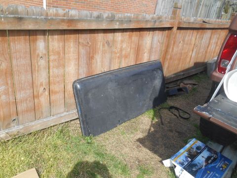 1972 Ford Bronco - A black tailgate rests on grass beside a wooden fence and part of a brown vehicle.