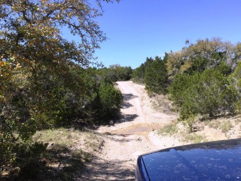 1996 Ford Bronco - A vehicle drives up a rough dirt path surrounded by trees under a clear blue sky.