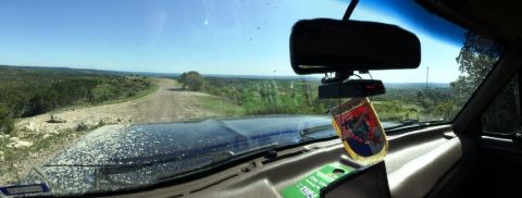 1996 Ford Bronco - Driving through a scenic, undeveloped area on a dusty dirt road. The view is expansive with rolling hills and scattered trees.