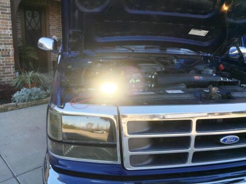 1996 Ford Bronco - The front grille and engine bay of a blue Ford truck are visible with the hood raised.