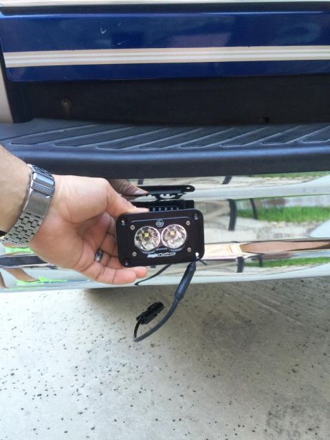 1996 Ford Bronco - A hand holds an aftermarket LED light bar near the chrome bumper of a blue vehicle.