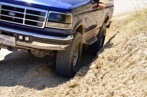 1996 Ford Bronco - 1996 Ford Bronco navigates a sandy trail, showing its off-road capability.