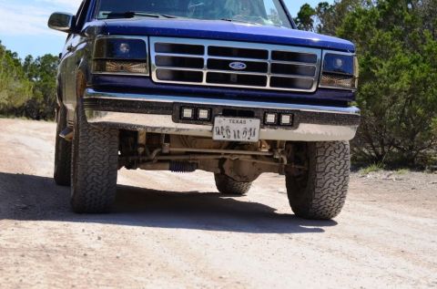 1996 Ford Bronco - This blue Ford truck has a prominent grille and aftermarket lights mounted on the front bumper.