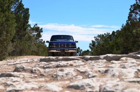1996 Ford Bronco - A blue Ford F-150 truck navigates a rough, rocky trail under a clear blue sky.