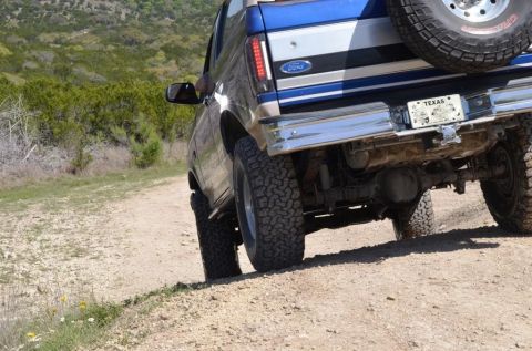 1996 Ford Bronco - Rear view of a 1996 Ford Bronco driving on a dirt path with a spare tire on the tailgate.