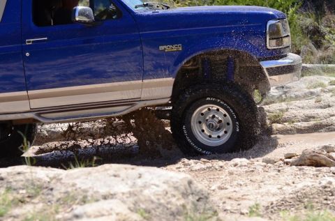 1996 Ford Bronco - A blue 1996 Ford Bronco navigates through a rocky stream, kicking up water.