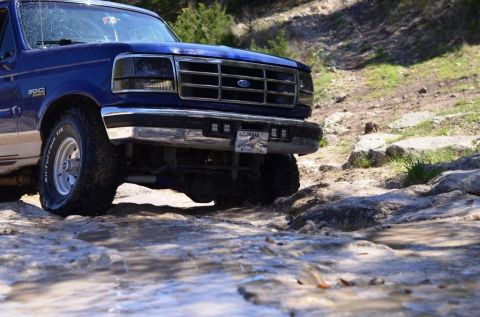1996 Ford Bronco - A blue Ford Bronco navigates a challenging off-road path with rocky obstacles.