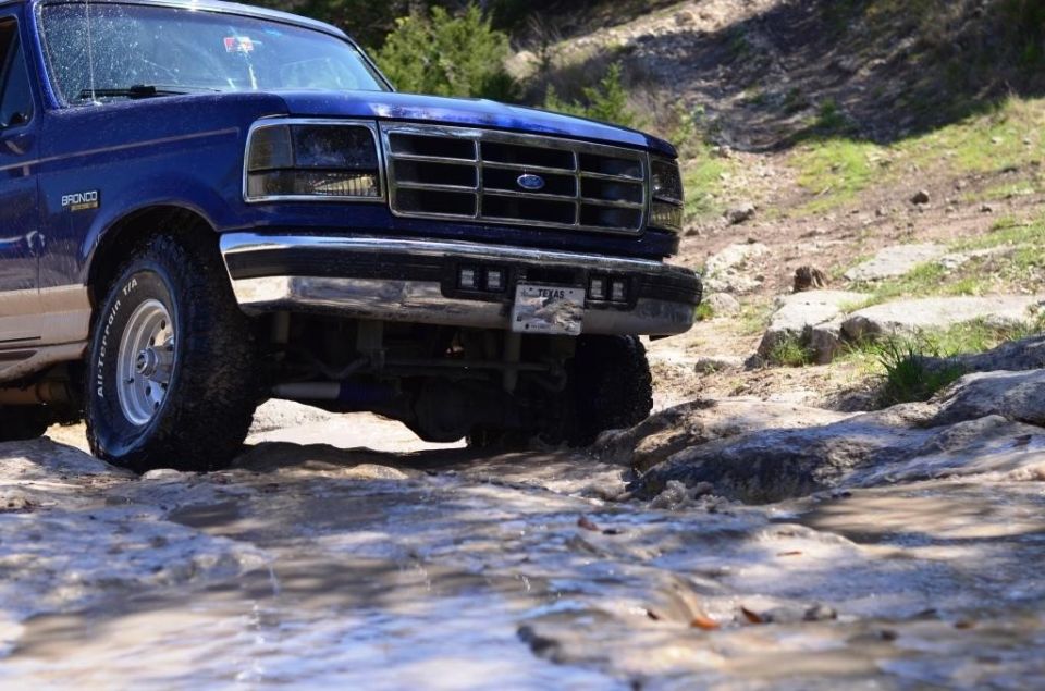 Blue Ford Bronco driving through rocky terrain, front 3/4 view