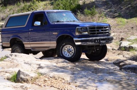 1996 Ford Bronco - This blue Ford Bronco navigates a rocky off-road path, its capability on challenging terrain.