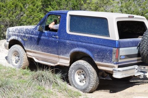 1996 Ford Bronco - This blue Ford Bronco, covered in mud, navigates an off-road trail.