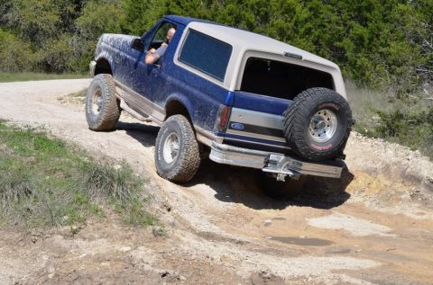 1996 Ford Bronco - Blue 1996 Ford Bronco navigates an off-road trail with a spare tire mounted on the back.