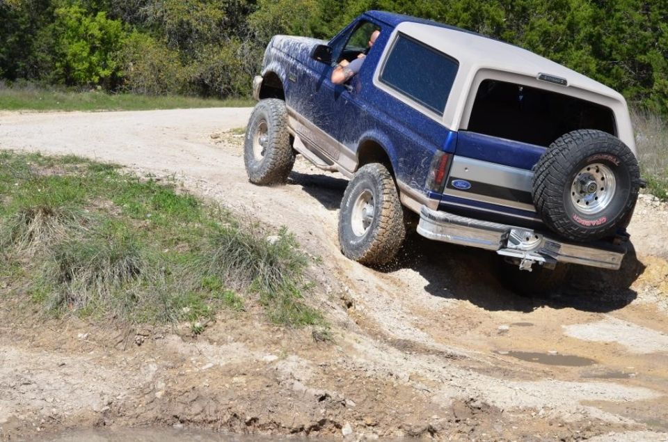 Blue Ford Bronco climbing a dirt hill with a spare tire on the back