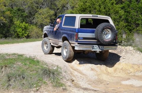 1996 Ford Bronco - A blue and tan Ford Bronco navigates a dirt path surrounded by trees.