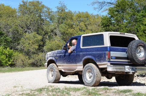 1996 Ford Bronco - Man driving a blue 1996 Ford Bronco on a dirt road, giving a thumbs up.