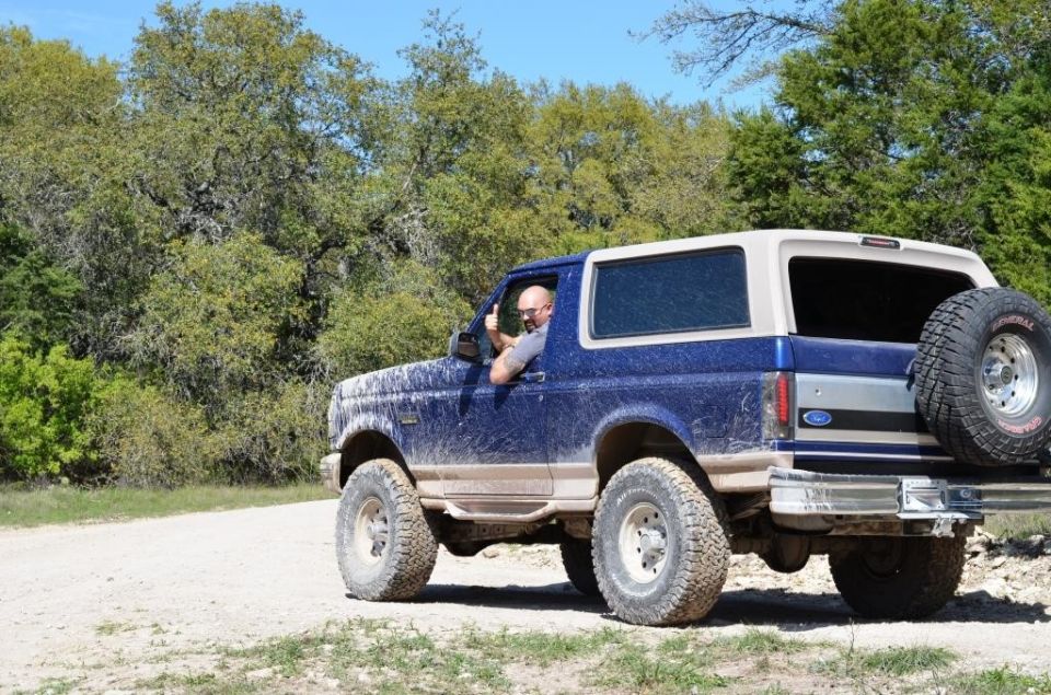 1996 Ford Bronco driving on a dirt road, driver gives thumbs up